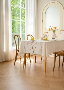 Close-up of embroidered pink flowers and tassel edge on cream rectangular tablecloth