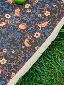 Close-up of woven jacquard floral fabric with bird motifs and white fringe on grass