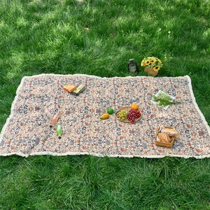 Outdoor picnic mat with vintage floral patterns and elegant fringe tassels on grass