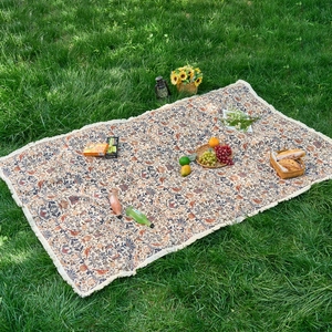 Close-up detail of vintage floral woven picnic mat with fringe tassels on green grass