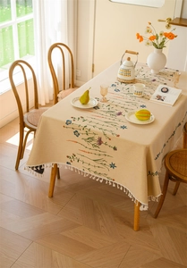 Detail of floral jacquard tablecloth with white cotton tassels on a rustic wooden table