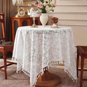 Elegant white lace tablecloth with leaf patterns and fringe tassels on a round wooden table