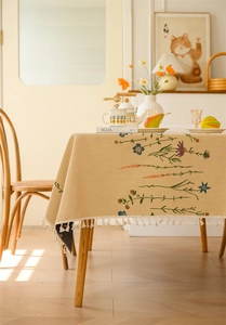 Detailed close-up of floral jacquard embroidery and tassel fringe on a rustic tablecloth