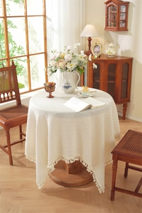 Detail of round beige tablecloth with textured crochet weave and decorative fringe tassels
