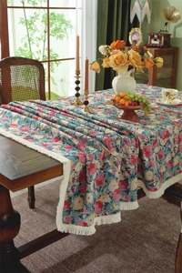Detail of vintage floral tablecloth with white fringe tassels on a rustic wooden table