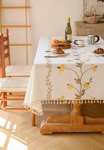 Detail of embroidered yellow daisies and tassels on a beige linen tablecloth texture