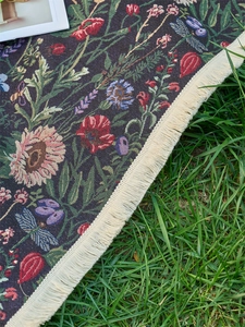Detail of floral jacquard woven picnic blanket with tassels on green grass lawn