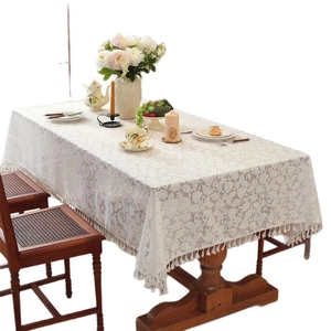 Elegant white lace tablecloth with floral patterns and tassels on a wooden dining table