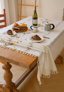 Detailed embroidery of yellow flowers and fringe tassels on cream rectangular tablecloth