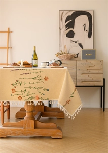 Detailed close-up of floral embroidery and fringe tassels on a beige table runner