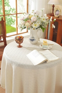 Close-up of beige round tablecloth with mesh texture and delicate tassel edges