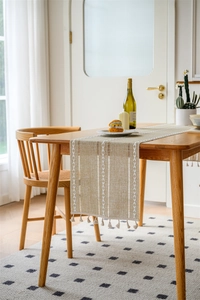 Detail of hollow jacquard table runner with embroidered leaves and handmade tassels