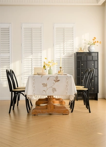 Detailed embroidery of brown leaves on cream tablecloth with elegant hanging fringe edges