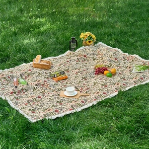 Detail of floral woven tablecloth with tassels and picnic accessories on green grass
