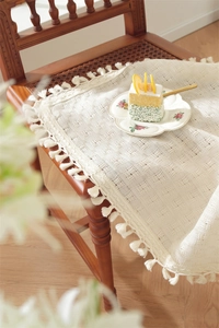 Detail of beige polyester tablecloth with thick fringe edges on a vintage chair