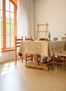 Close-up of beige jacquard floral tablecloth with elegant tassel edges on a wooden table