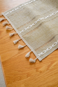 Detail of jacquard hollow table runner with white embroidery and handmade tassels