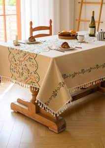 Close-up of beige woven tablecloth featuring floral jacquard embroidery and cream fringe