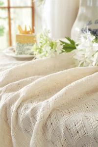 Close-up of cream woven tablecloth with fringe tassel and delicate mesh texture details