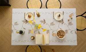 Detail of embroidered vine leaf patterns on a cream linen-textured rectangle tablecloth