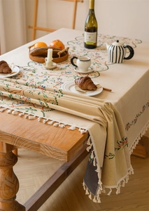 Detailed embroidery on a beige floral tablecloth with decorative white tassels and a cozy vibe