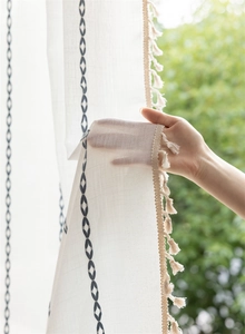 Detail of geometric blue embroidery and beige tassels on white translucent polyester curtain