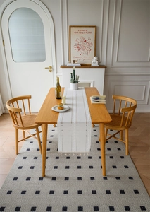 Detail of white jacquard table runner with fringe on a wooden table with rattan chairs