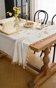 Close-up of beige linen tablecloth with floral embroidery and tassel fringe details