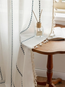 Detail of bohemian cream curtain with blue embroidery and decorative cotton fringe