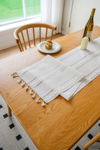 Detail of hollow woven table runner with tassels on a natural wooden dining table