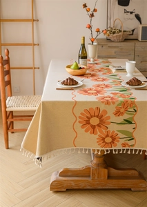 Close-up of beige jacquard tablecloth featuring orange daisy patterns and white fringe tassels