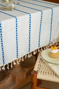 Detail of bohemian cream tablecloth with blue embroidery lines and fringe on wood table