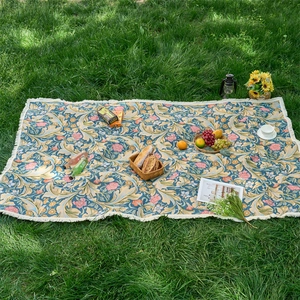 Close-up of floral outdoor picnic mat with tassels on green grass with picnic props