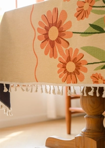 Close-up of woven floral tablecloth with orange daisy print and delicate fringe edges