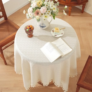 Beige waffle weave round tablecloth with fringe tassels on a wooden dining table