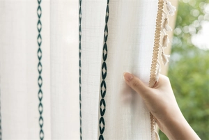 Detail of white jacquard curtain with green geometric embroidery and beige tassels