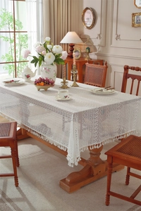 Detail of white lace tablecloth featuring geometric hollow patterns and pompom fringe