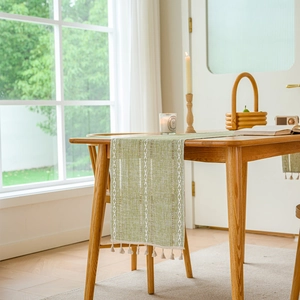 Detailed texture of green jacquard table runner with geometric weave and tassels
