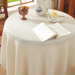 Beige round waffle weave tablecloth with pom-pom fringe on a wooden dining table