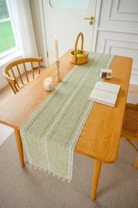 Detailed weave texture of green table runner with white diamond embroidery and tassels