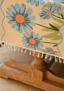 Detail of beige tablecloth with blue daisy pattern and off-white tassel fringe edge