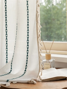 Detail of linen texture curtain with green embroidery and handmade tassels by window