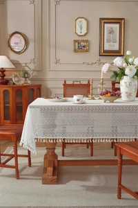 Detailed close-up of white lace tablecloth with hollow patterns and fringe tassels
