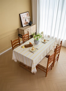 Detailed close-up of cream textured tablecloth with yellow stripes and tassel edge