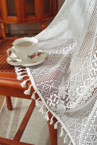 Detail of white hollow floral lace tablecloth with fringe edge on a vintage chair