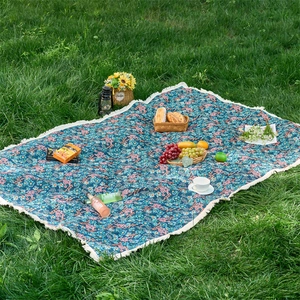 Close-up of floral jacquard picnic blanket with white tassels on lush green grass