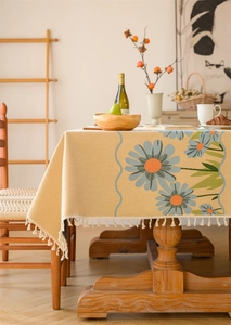 Close-up of rustic woven tablecloth featuring blue daisy patterns and soft cream fringes