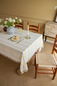 Detail of bohemian yellow striped tablecloth featuring elegant off-white tassel edges