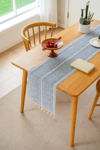 Detail of blue jacquard table runner with white chain embroidery and beige tassel fringe