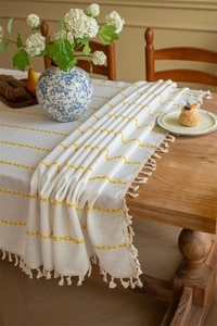Detail view of white jacquard tablecloth featuring yellow heart embroidery and tassel edges